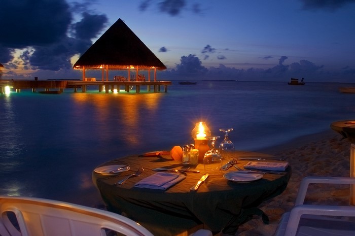 Cancun travel guide: Romantic candlelit dinner setup on the beach at sunset, with a palapa in the background and the sea and sky creating a romantic atmosphere in Cancún.