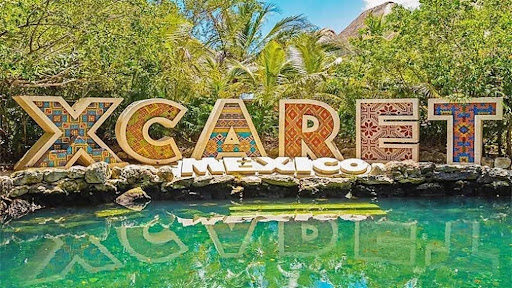 Cancun travel guide: Xcaret Mexico sign with palm trees in the background and emerald-colored water beneath it, offering a glimpse of the natural beauty of the region.
