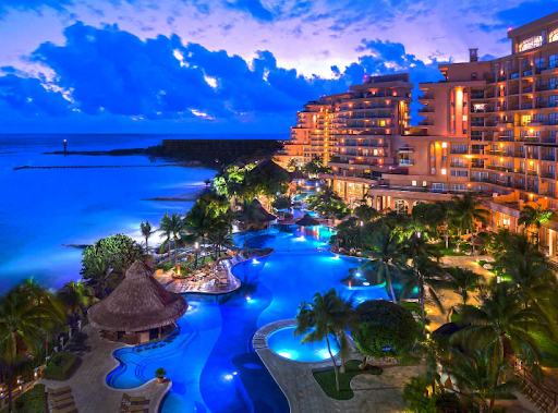 Cancun travel guide: A beautiful hotel at sunset with illuminated pools, palm trees, and a stunning view of the Caribbean Sea in the Hotel Zone.
